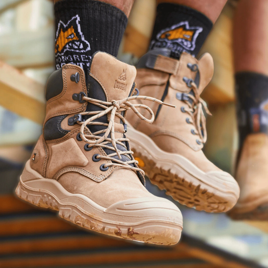 Stone Mongrel Safety Boots with a zip and laces, black socks with the Mongrel logo, and a blurred background.